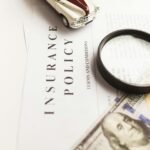 Close-up image of an insurance policy with a magnifying glass, money, and toy car.